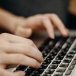 Close-up shot of hands typing on a laptop keyboard in a work environment.